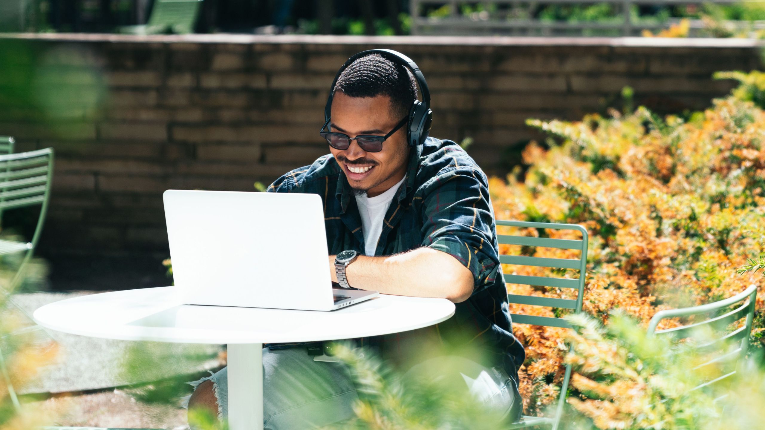 Man sitting outdoors, wearing headphones, and smiling at laptop camera