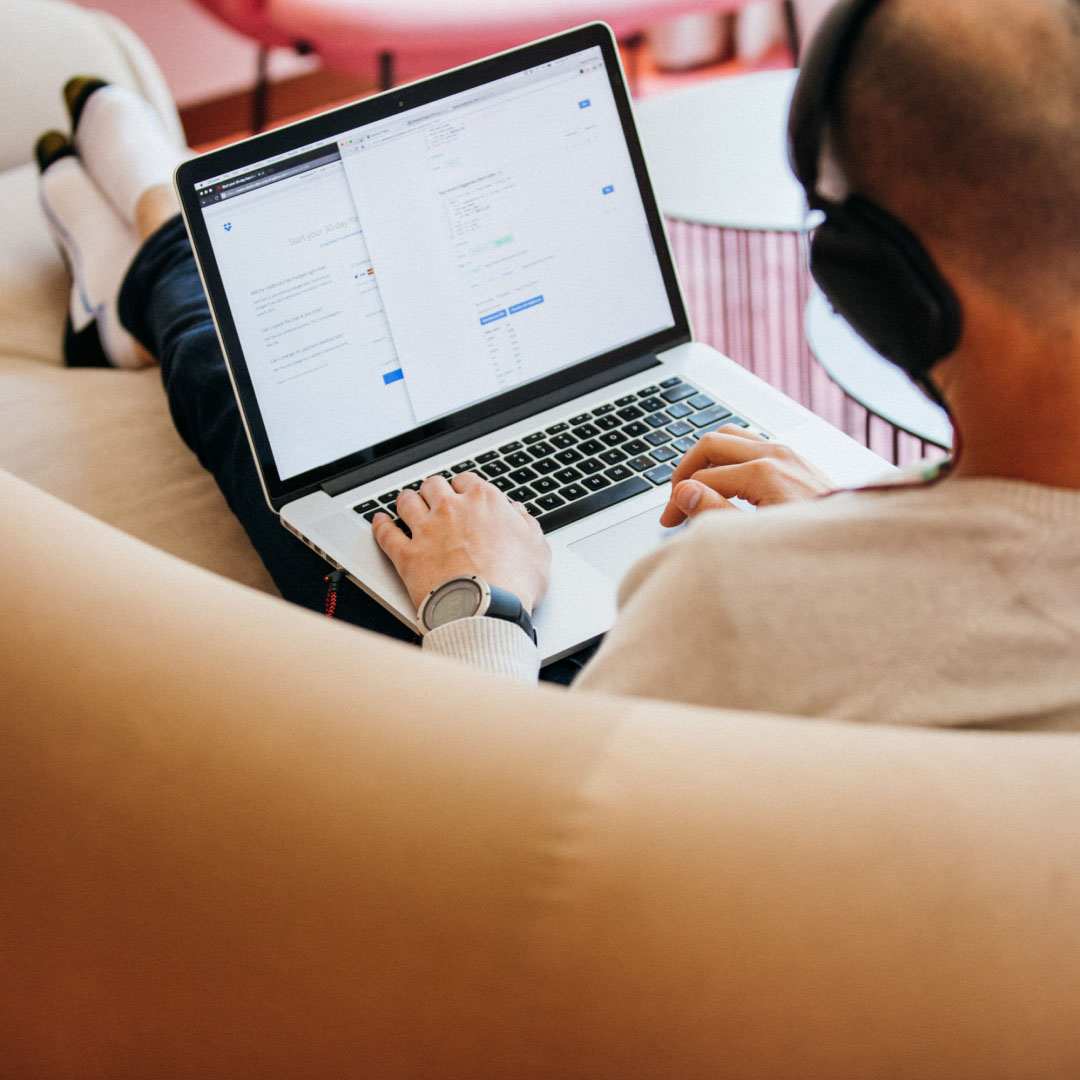 Persona che lavora in remoto indossando le cuffie mentre lavora su un laptop, seduta con i piedi sul divano
